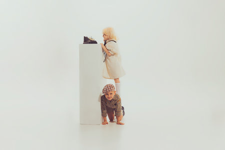 Portrait of little boy and girl, children playing together, trying to reach vintage phone isolated over grey background. Concept of childhood, friendship, fun, lifestyle, fashion, retro styleの写真素材