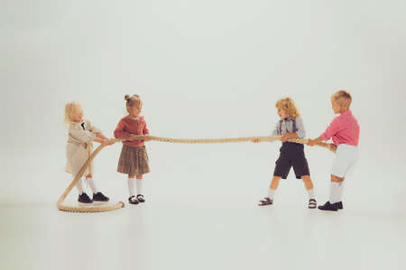 Portrait of children, boys and girls playing together, pulling the rope isolated over grey studio...