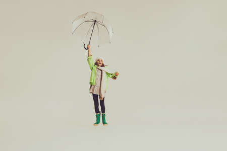 Portrait of girl, child in autumn outfit jumping under umbrella isolated over grey studio background. Concept of childhood, friendship, fun, lifestyle, autumn fashion, retro styleの写真素材