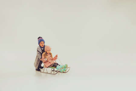 Portrait of boy and girl, children in winter clothes sledding isolated over grey studio background. Winter holidays. Concept of childhood, friendship, fun, lifestyle, fashion, retro styleの写真素材