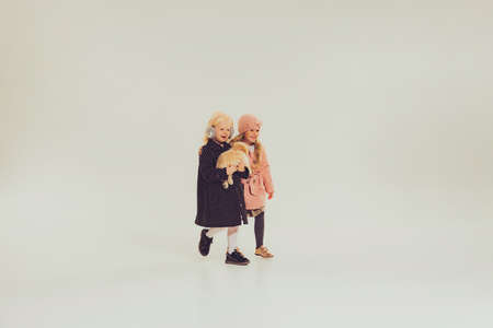 Portrait of two little girls, children in winter clothes walking together with dog isolated over grey studio background. Concept of childhood, friendship, fun, lifestyle, fashion, retro styleの写真素材