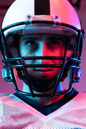Close-up portrait of young man, american football player in helmet posing isolated over purple background neon light. Concept of active life, team game, energy, sport, competition. Copy space for adの写真素材