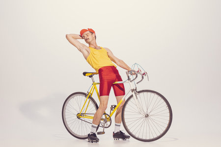 Portrait of young man in colorful clothes, uniform riding bike isolated on grey background. Looking relaxed. Chilling. Concept of sport, hobby, work, active lifestyle, retro fashion. Copy space for adの写真素材