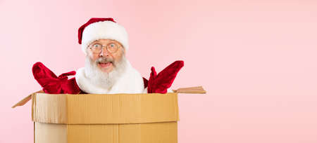 Portrait of cheerful senior man, Santa Claus sitting inside cardboard box. Happy Holidays. Delivery...