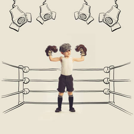 Portrait of little boy pretending to be professional boxer, standing on drawn ring in big brown gloves. Concept of childhood, dreams, creativity, fun, lifestyle, retro styleの写真素材