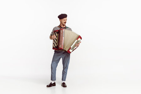 Portrait of young man playing accordion, posing isolated over white studio background. Countryside music. Concept of live music, performance, retro style, creativity, artistic lifestyleの写真素材