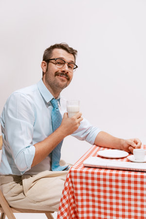Portrait of smiling man in official clothes sitting at the table and heaving breakfast. Looks calm...