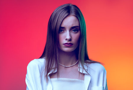 Portrait of young beautiful woman posing, looking at camera with sadness isolated over red background in neon light. Concept of beauty, lifestyle, youth, emotions, facial expression, ad.の写真素材