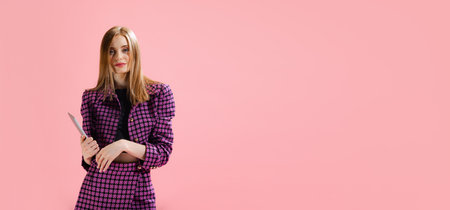 Portrait of young beautiful woman posing in stylish classical suit with laptop isolated on pink studio background. Business woman. Concept of beauty, lifestyle, youth, emotions, facial expression, ad.の写真素材