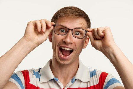 Portrait of young man in glasses posing isolated over white studio background. Crazy face. Good mood. Concept of emotions, facial expression, lifestyle, youth. Copy space for adの写真素材