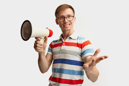Portrait of young man in glasses posing with megaphone isolated over white studio background. Good proposal. Concept of emotions, facial expression, lifestyle, youth. Copy space for adの写真素材