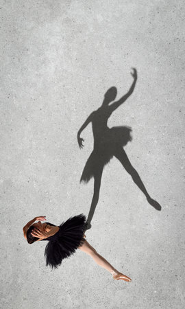 Portrait of young ballerina in black dress dancing isolated over grey wall background. Top view. Shadow element. Concept of classic ballet, inspiration, beauty, dance, creativityの写真素材