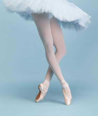 Cropped image of female legs, ballerina in tutu and pointe standing on tiptoe isolated isolated over blue studio background. Concept of classic ballet, inspiration, beauty, dance, creativityの写真素材