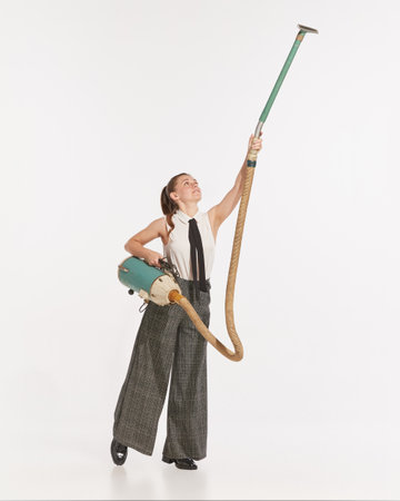 Portrait of young woman cleaning with vintage vacuum cleaner isolated over white studio background. Concept of retro fashion, style, creativity, youth culture, emotions, adの写真素材