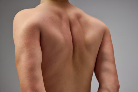 Cropped image of male muscular back. Model posing shirtless isolated over grey studio background. Pains in back, spine. Concept of mens health, natural beauty, body and skin care.の写真素材