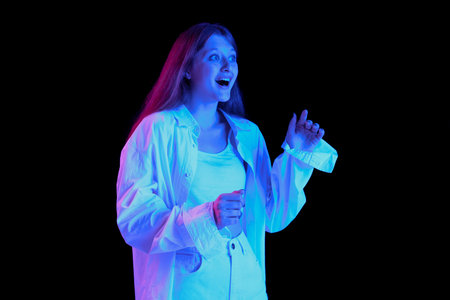Portrait of young beautiful girl posing in white casual clothes isolated on black background in blue...