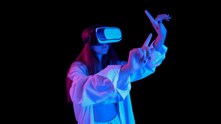 Portrait of young beautiful girl posing in VR glasses isolated over black background in blue neon...