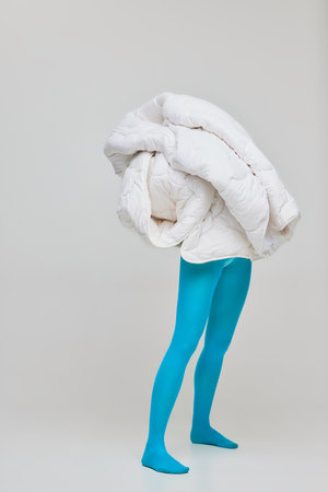 Portrait of young girl in blue tights covered in white blanket isolated over grey studio background. Feeling warm and safe . Concept of retro fashion, art photography, style, queer, beauty, adの写真素材