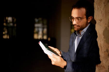 Portrait of businessman standing at the wall in empty room with notebook. Making professional analytics and countings to open new business. Concept of business, challenges, work, occupationの写真素材