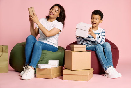 Portrait of woman sitting with teen boy and unpacking boxes after shopping isolated over pink background. Concept of shopping, online order and delivery, Black Friday sales. Copy space for ad, textの写真素材
