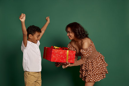 Portrait of young woman giving box present box to teen boy over green background. Holiday gifts. Concept of shopping, online order and delivery, Black Friday sales. Copy space for ad, textの写真素材