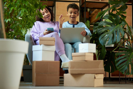 Portrait of cheerful woman and teen boy doing online shopping at home on laptop. Delivery of boxes....