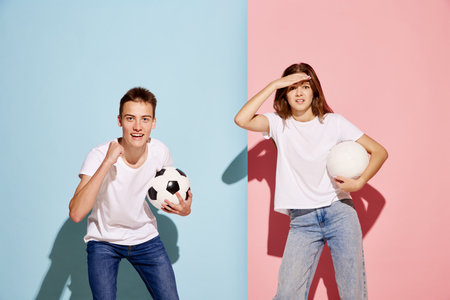 Portrait of young man and woman, sport fans posing with football ball isolated over blue-pink background. Emotional. Concept of youth culture, fashion, relationship, emotions. Copy space for adの写真素材