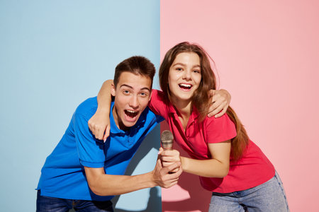 Portrait of young people, man and woman posing with microphone isolated over blue-pink background. Karaoke singers. Concept of youth culture, fashion, relationship, emotions. Copy space for adの写真素材