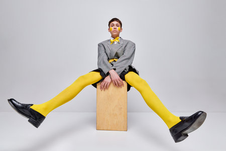Portrait of stylish boy posing in jacket, blazer and yellow tights isolated over grey background....
