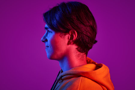 Portrait of young man in casual hoodie posing, looking away isolated over purple background in neon light. Side view. Concept of youth, casual fashion, facial expression, emotions, lifestyle, adの写真素材