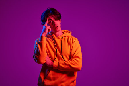 Portrait of young man in casual hoodie posing with thoughtful face isolated over purple background in neon light. Concept of youth, casual fashion, facial expression, emotions, lifestyle, adの写真素材
