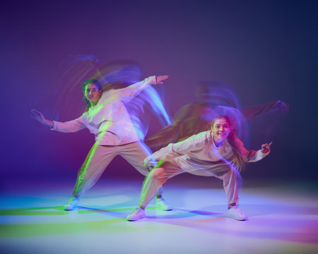 Portrait of young girls dancing hip-hop isolated over gradient blue purple background in neon with mixed light. Hobby. Concept of movement, youth culture, active lifestyle, action, street danceの写真素材