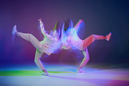 Two young girls dancing hip-hop isolated over gradient blue purple background in neon with mixed...