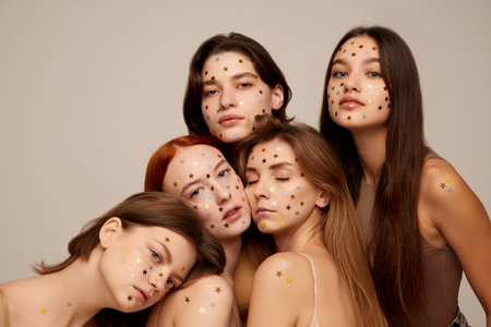 Portrait of five young beautiful women posing in beige underwear isolated over grey background. Stars glitter on face. Concept of beauty, freedom, emotions, extraordinary fashion, modern style, youthの写真素材