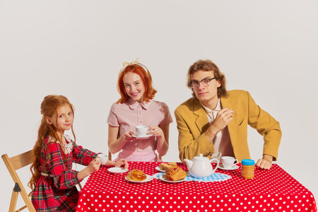 Family breakfast. Portrait of young woman, man and little girl sitting at the table isolated on grey background. Concept of beauty, retro style, fashion, elegance, 60s, 70s, family. Copy space for adの写真素材