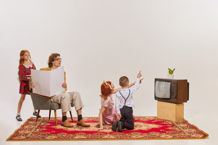 Portrait of young family watching TV isolated over grey background. Cheerful time together . Concept of beauty, retro style, fashion, elegance, 60s, 70s, family. Copy space for adの写真素材