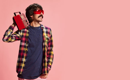 Stylish man with moustache posing in red sunglasses, checkered shirt and vintage radio player isolated over pink background. Concept of retro style, creativity, emotions, facial expression, fashionの写真素材