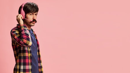 Portrait of stylish man with moustache posing in headphones isolated over pink background. Flyer. Communication. Concept of retro style, creativity, emotions, facial expression, fashionの写真素材