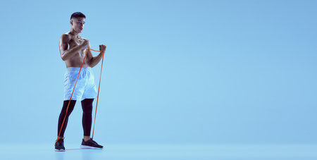Portrait of young muscular man training with sports expander isolated over blue background in neon light. Flyer image. Concept of sport, fitness, healthy and active lifestyle, motivation, workoutの写真素材