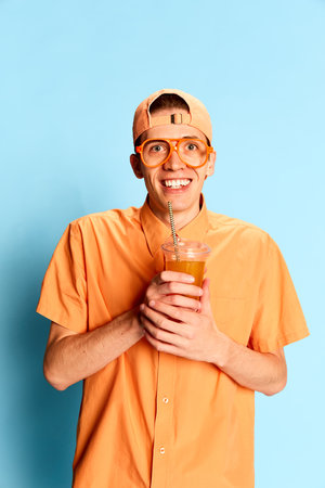 Tasting lemonade. Portrait of young emotional man in casual clothes and cap isolated over light blue background. Concept of feelings, youth, fashion, facial expression, emotions, lifestyle, adの写真素材