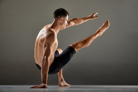 Portrait of male flexible muscular athlete showing animal flow sport elements isolated over gray background. Yoga, fitness, trendy sports, beauty of body. Grace and flexibility of human bodyの写真素材