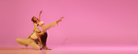 Two stylish female dancers in casual style clothes dancing contemporary choreography dance isolated over crystal pink background. Concept of modern art, creativity, fusion. Emotions in movesの写真素材
