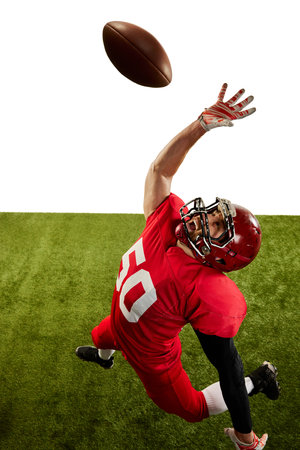 Aerial view of american football player in sports uniform and protective helmet catching ball isolated over white green background. Concept of professional sport, team, competition, championshipの写真素材
