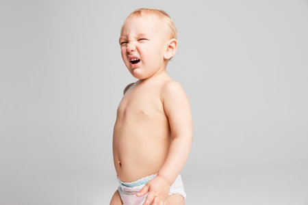 Grimace. Funny toddler boy, baby in diaper having fun isolated over grey studio background. Concept of happy childhood, motherhood, life, birth and health. Banner with copy space for adの写真素材