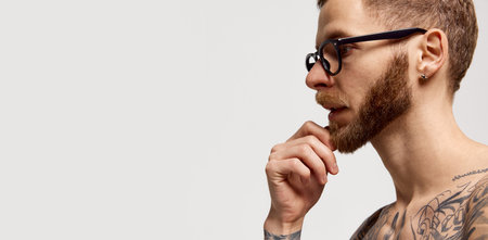 Close up portrait of charming bearded man in eyewear looking at camera confidently over grey...