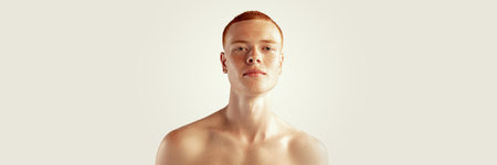 Handsome young red-haired man posing isolated over grey studio background. Male natural beauty. Concept of mens health, posing, beauty, body and skin care. Horizontal bannerの写真素材