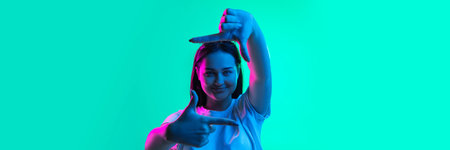 Pleasant emotions. One young beautiful girl demonstrating frame gesture isolated over light green...