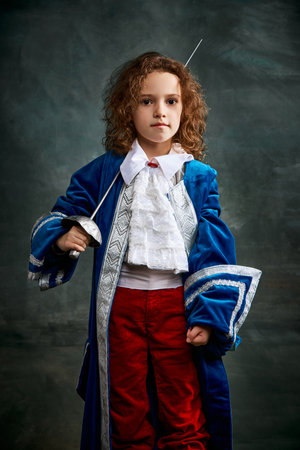 Cinematic portair of beautiful little girl dressed up as medieval knight, little prince over dark vintage style background, Fashion, beauty, emotions, theater concept. Eras comparisonの写真素材