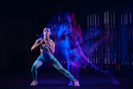 Squats. Sportive woman in sportswear and sportsfoot training in modern fitness room over dark background with mixed neon light. Active and healthy lifestyle conceptの写真素材