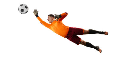 Young man, soccer football goalkeeper in sports uniform and boots catches ball in jump isolated over white background. Concept of sport, action, motion, goals.の写真素材